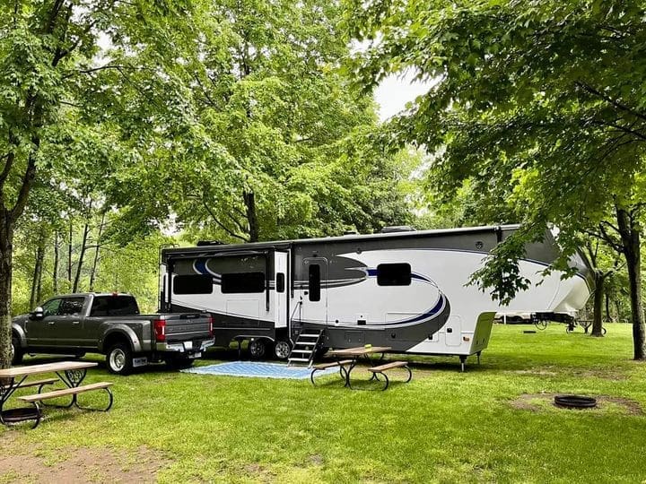 Luxe Fifth Wheel RV and pickup truck parked at a campsite, surrounded by green trees and grass